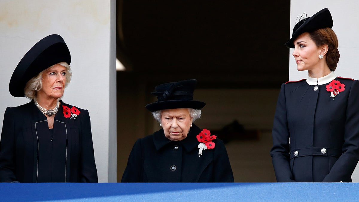 Queen Camilla and Kate Middleton looking at each other in black in between Queen Elizabeth