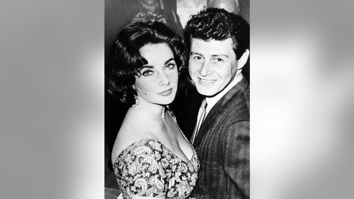 A close-up of a glum Elizabeth Taylor posing next to a smiling Eddie Fisher