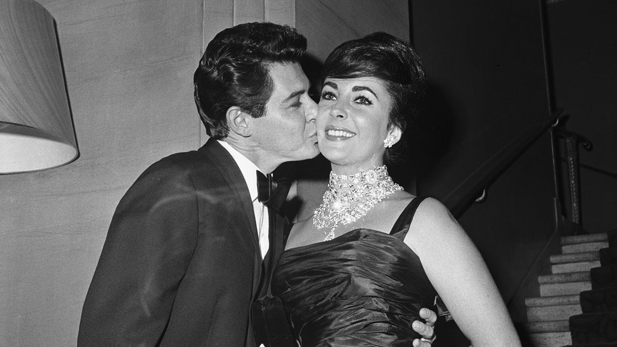 Eddie Fisher kissing Elizabeth Taylor on the cheek as she wears jewels and a glamorous gown.