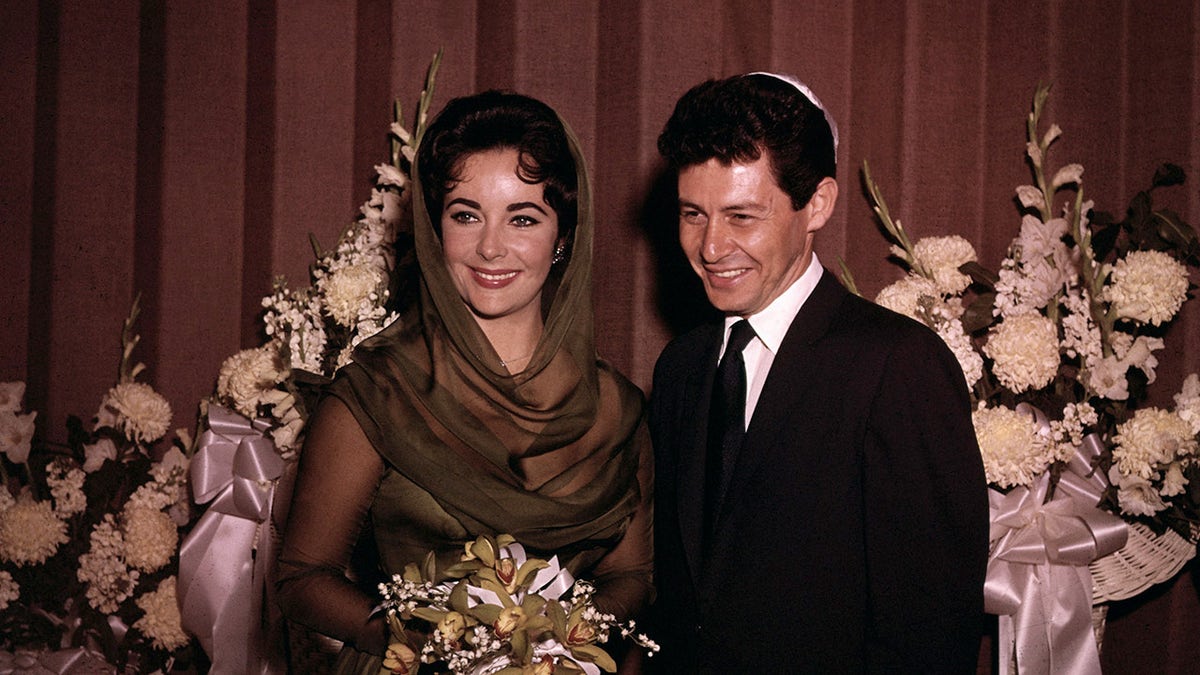 Elizabeth Taylor smiling in a dark bridal gown with Eddie Fisher on their wedding day.