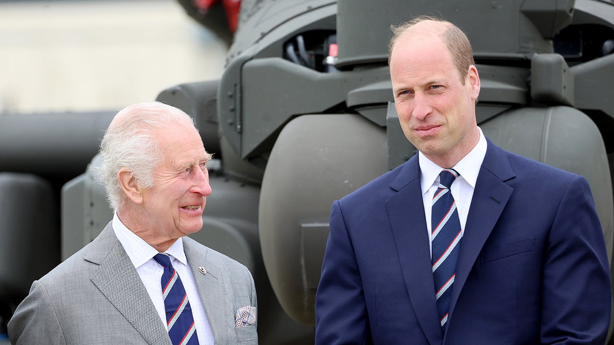 A close-up of King Charles wearing a grey blazer looking at his son Prince William in a blue blazer. They both are wearing striped ties.