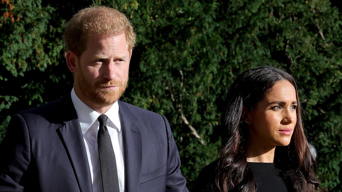 El príncipe Harry, con traje azul marino, y Meghan Markle, con vestido negro, muy serios.