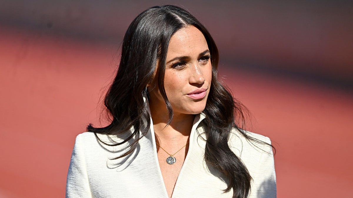 Meghan Markle mirando a un lado con un blazer marfil.