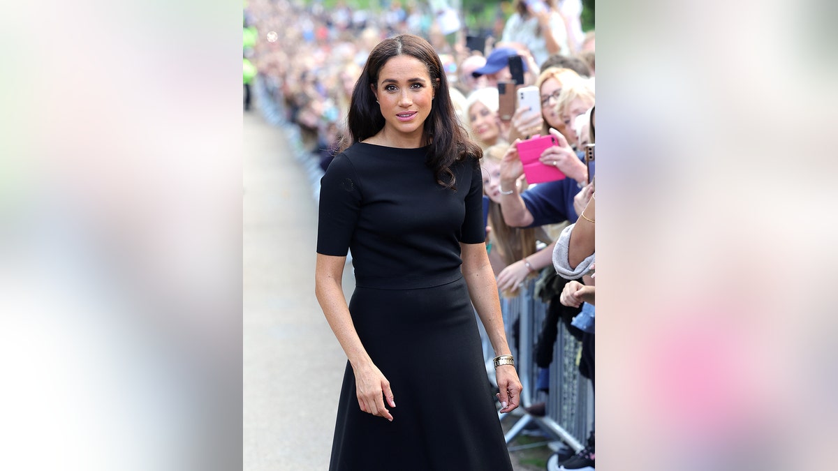 Meghan Markle wearing a back dress standing in front of a crowd.