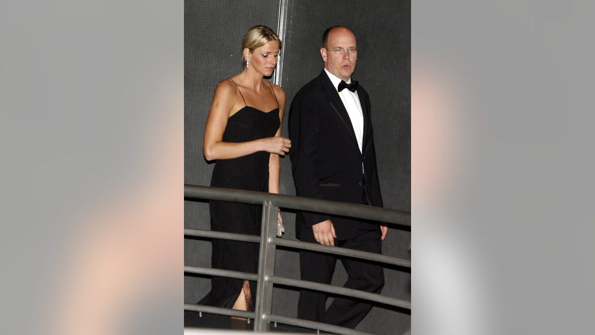 Princess Charlene wearing a strappy black dress next to Prince Albert in a suit and bow tie.