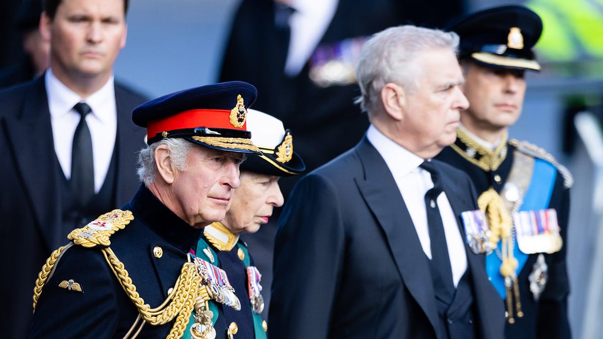 Prince Andrew walking forward in a suit in front of King Charles and Princess Anne.