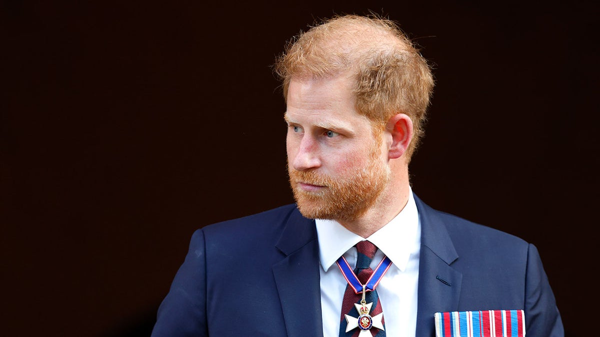 Príncipe Harry olhando para o lado em um terno azul-marinho adornado com medalhas.