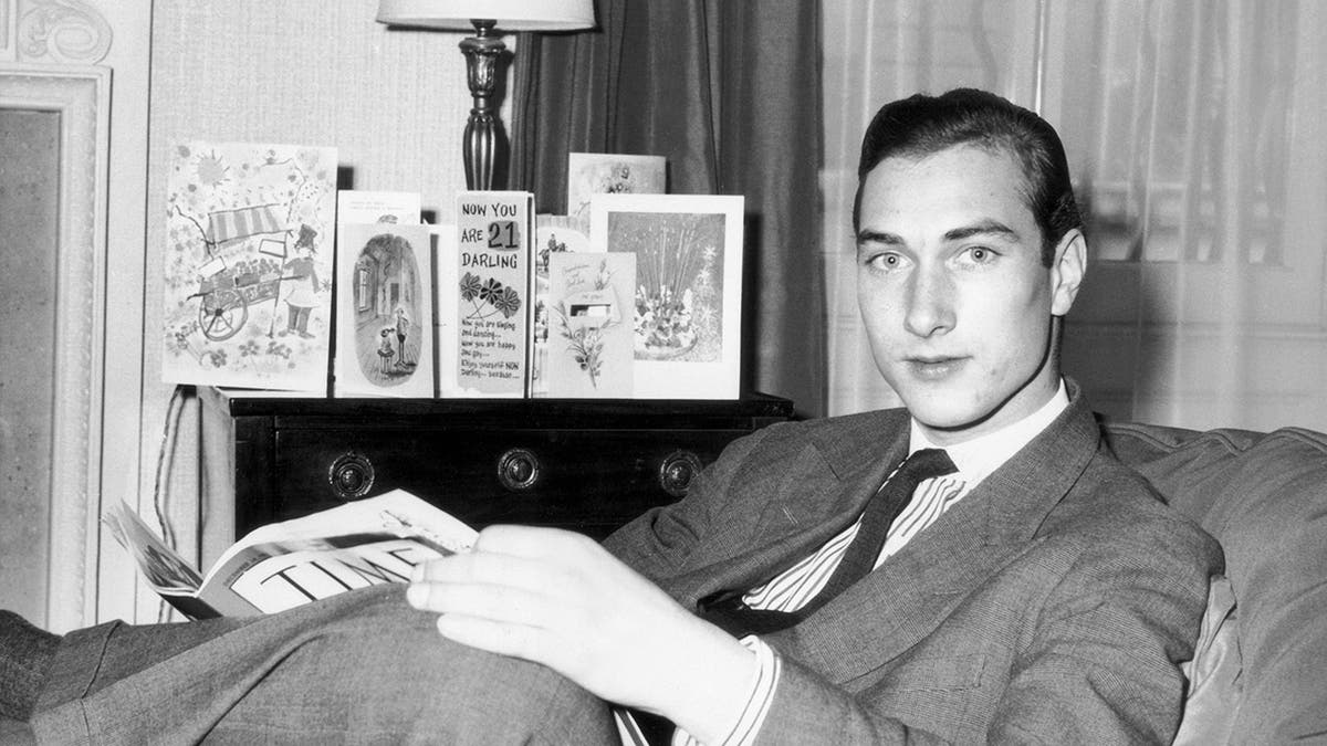 Prince William of Gloucester relaxing on a chair in front of greeting cards.