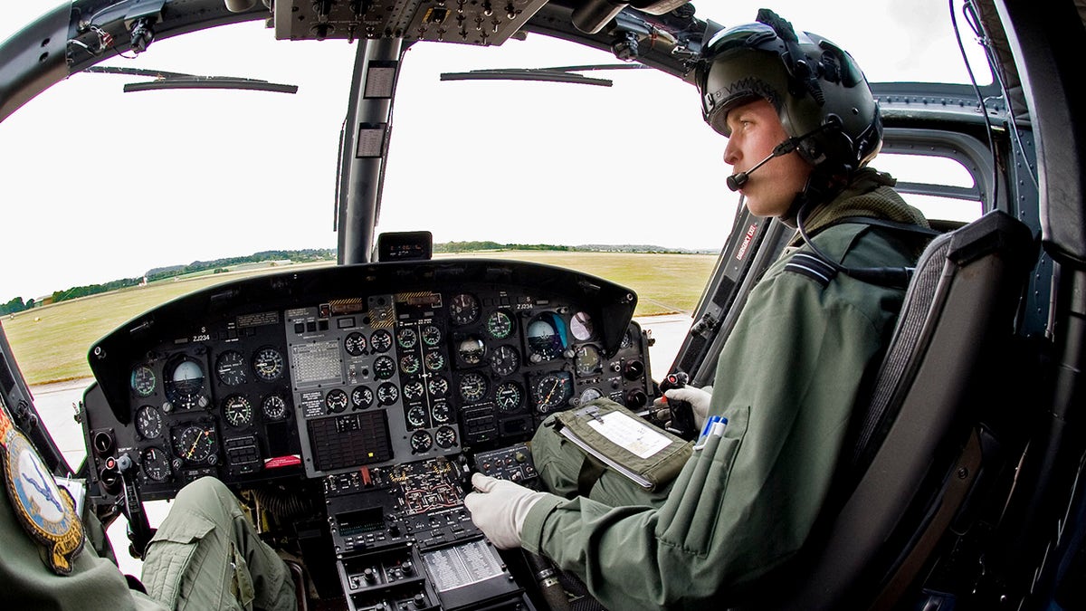 Prince William in uniform sitting in front of a helicopter.
