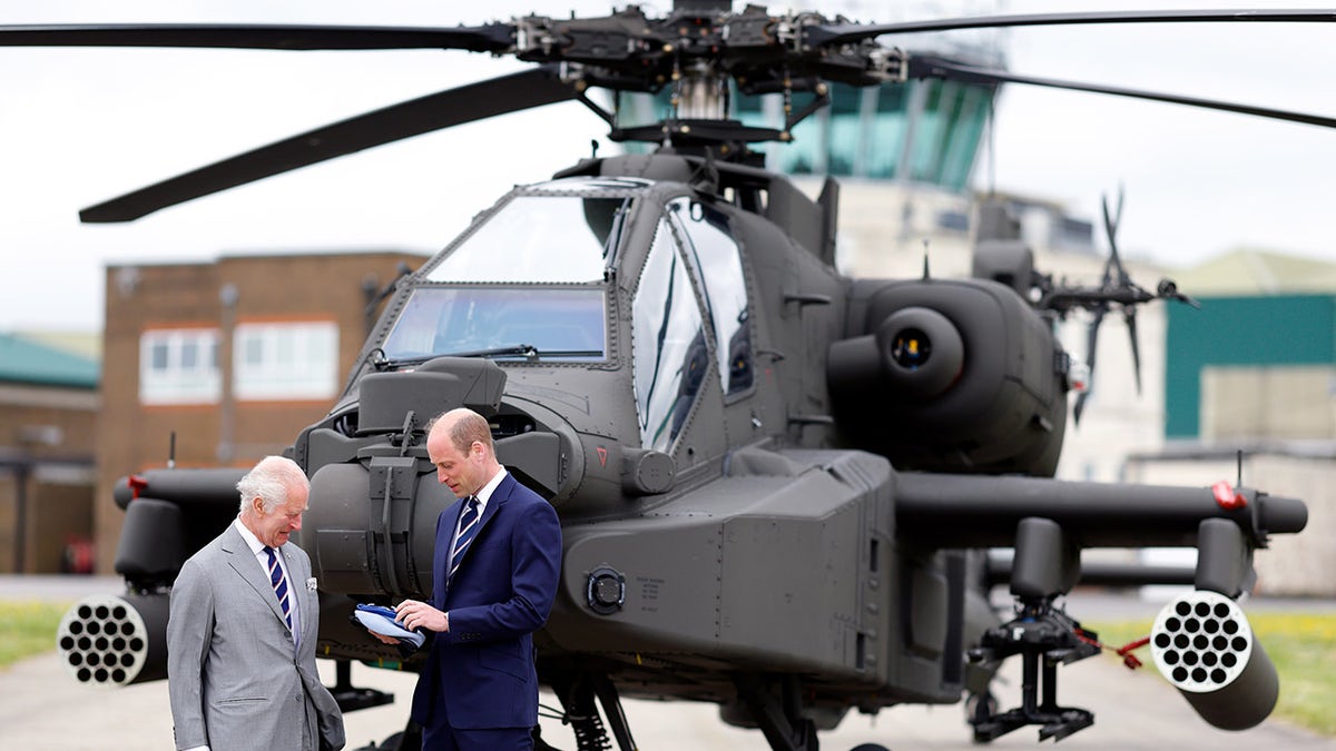 King Charles and Prince William chatting and looking down in front of a helicopter.