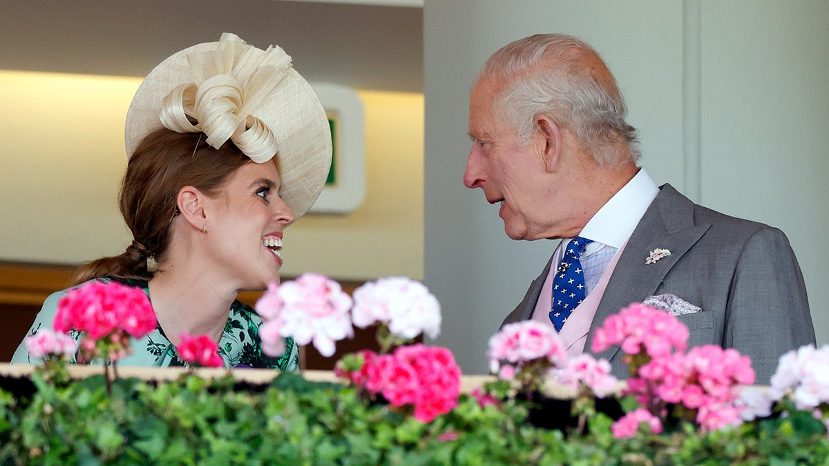 Princess Beatrice chatting with King Charles III against a row of flowers.