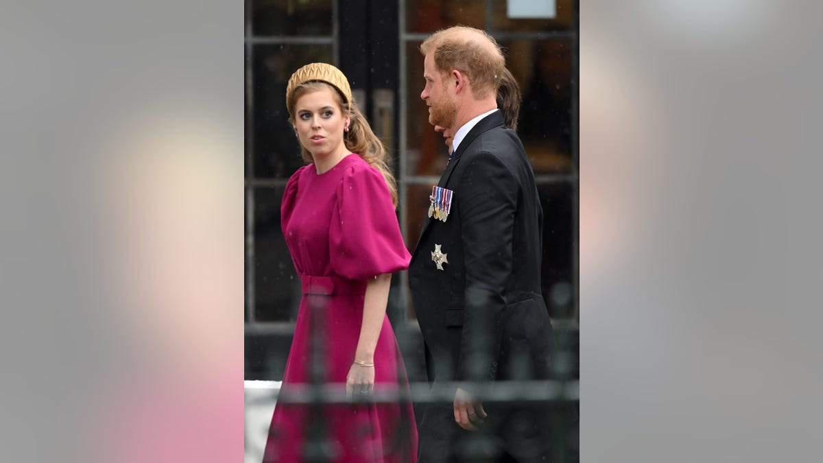 Princess Beatrice wearing a fuchsia dress with a gold tiara walking alongside Prince Harry.