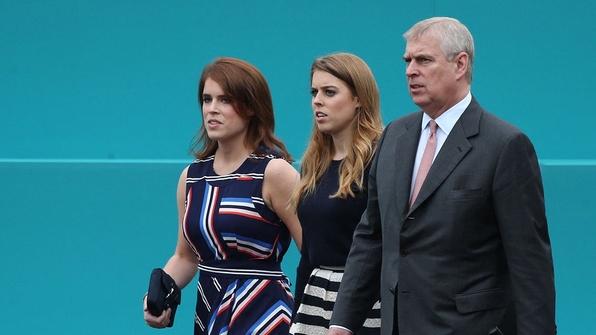 Princess Eugenie in a striped dress walking alongside Princess Beatrice in a black sweater and striped skirt and Prince Andrew in a grey suit.