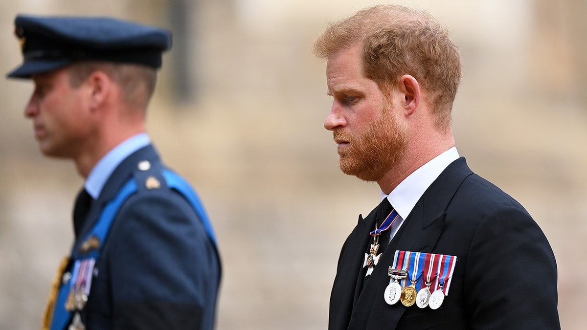 El príncipe Harry con traje y medallas caminando detrás del príncipe Guillermo de uniforme.