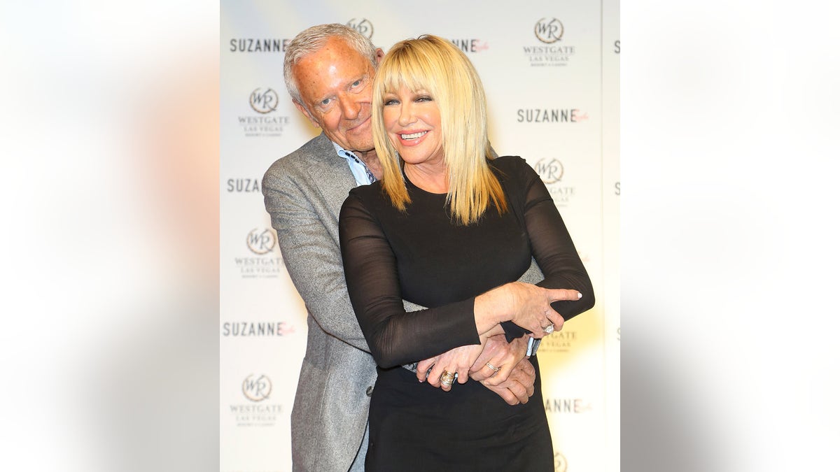 Alan Hamel wearing a grey suit embracing Suzanne Somers in a black dress.