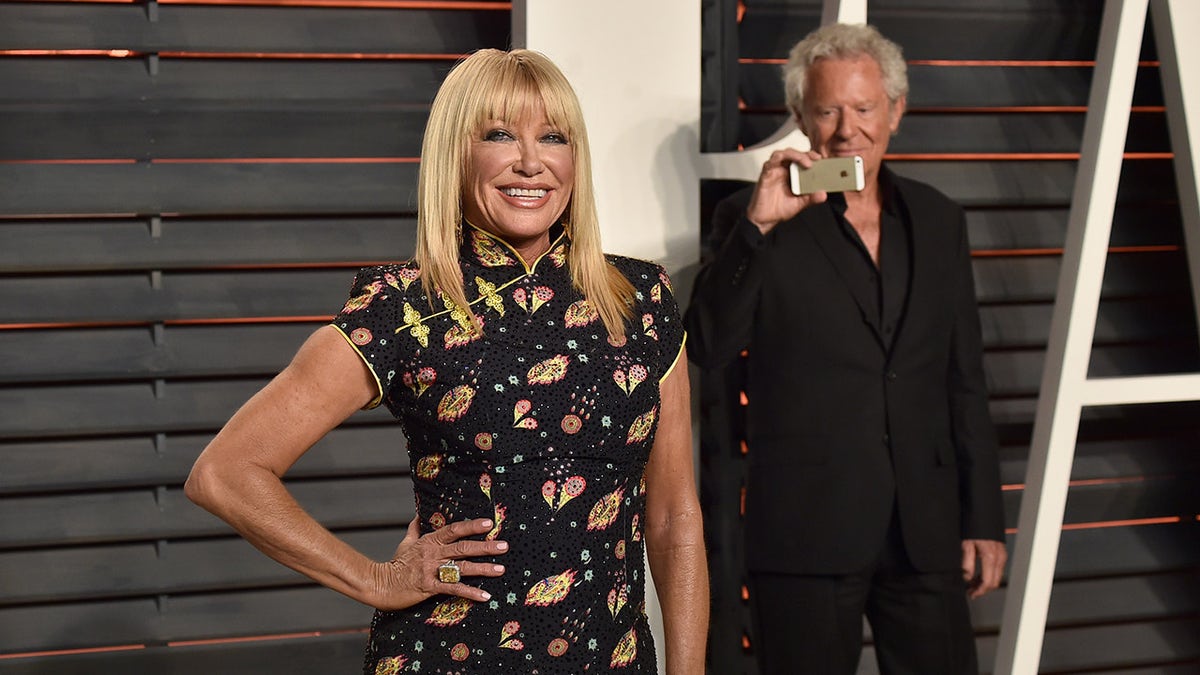 Alan Hamel recording Suzanne Somers as she smiles on the red carpet.
