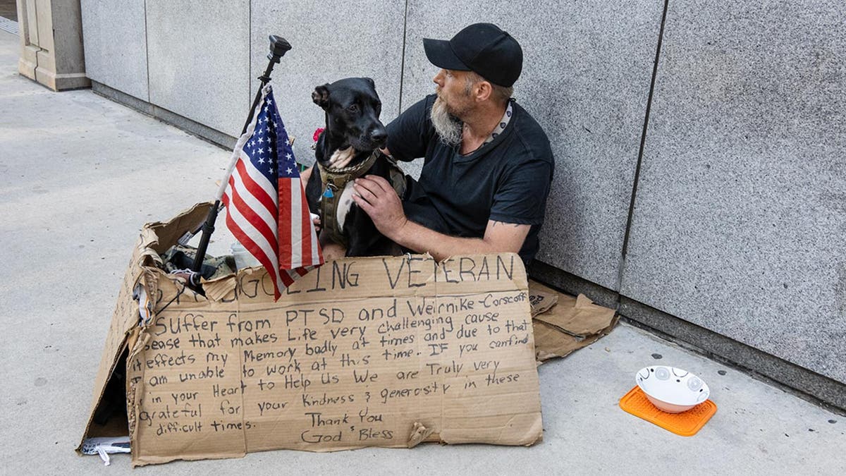 Um veterano sem-teto em Chicago com seu cachorro e uma placa de papelão está encostado na parede enquanto a Convenção Nacional Democrata está prestes a começar