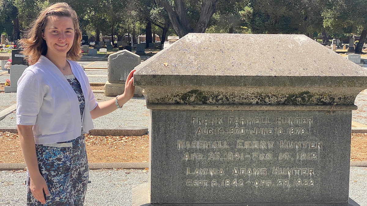 Young woman stands next to a war memorial in a cemetery. 