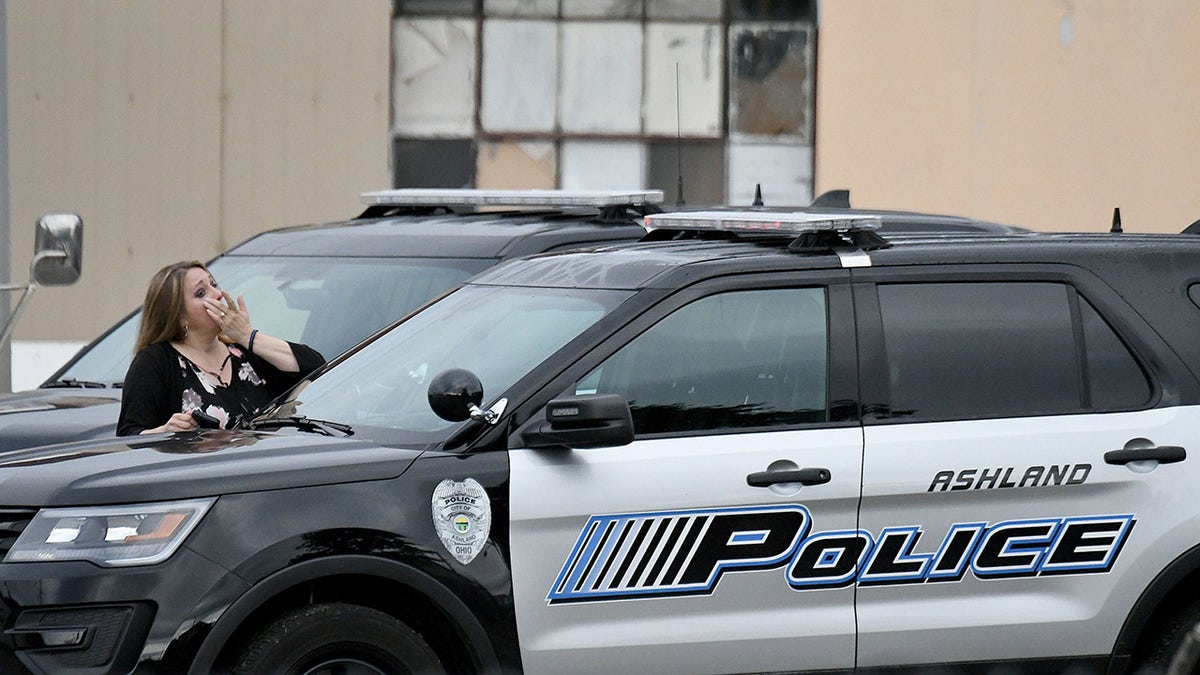 Kim Mager looking emotional in front of a police car wearing black.