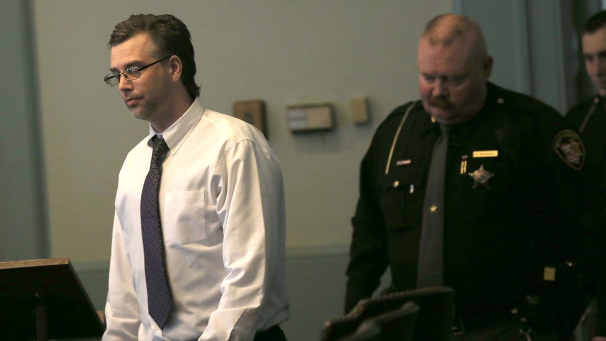 Shawn Grate walking away from a police officer wearing a white shirt and a dark blue tie.
