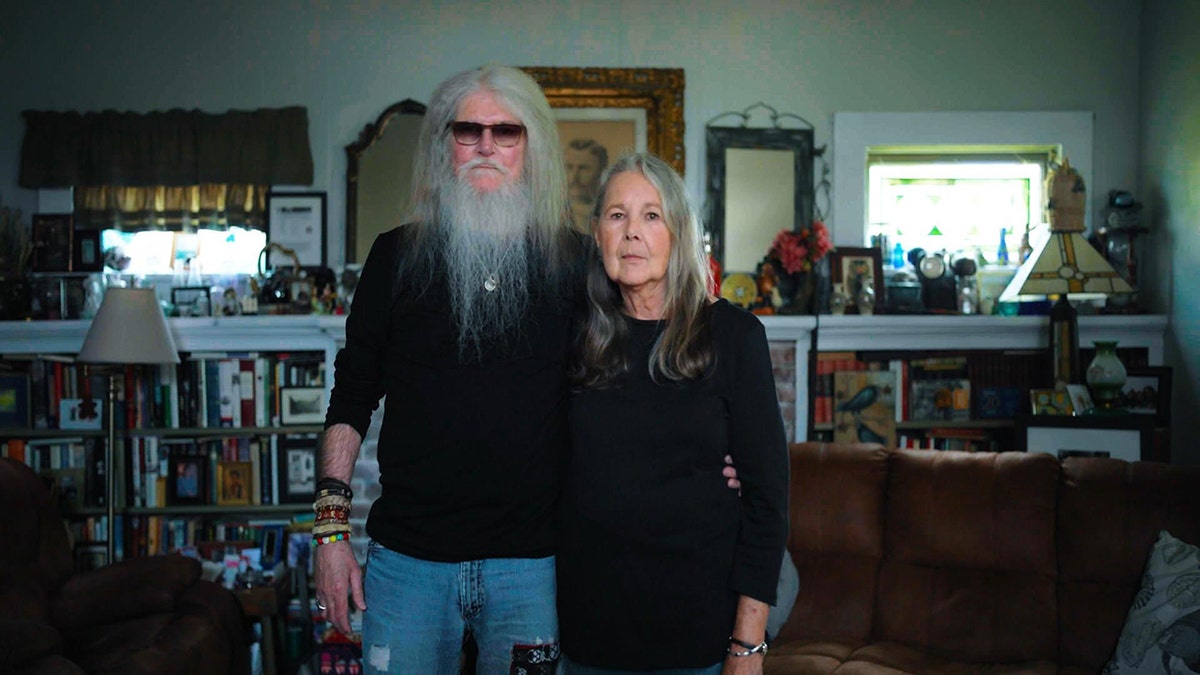 Jack Truitt poses with his wife Jackie Truitt while wearing matching black sweaters at home.