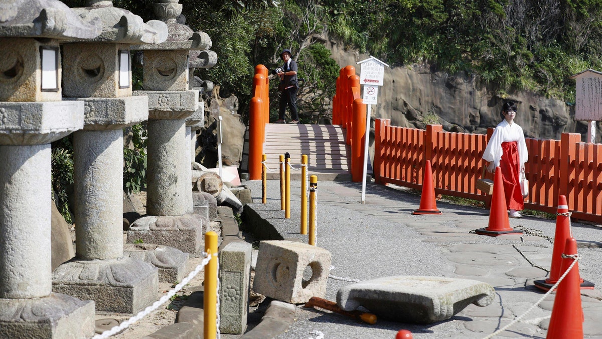 Una linterna de piedra caída rodeada de conos y cinta de precaución.