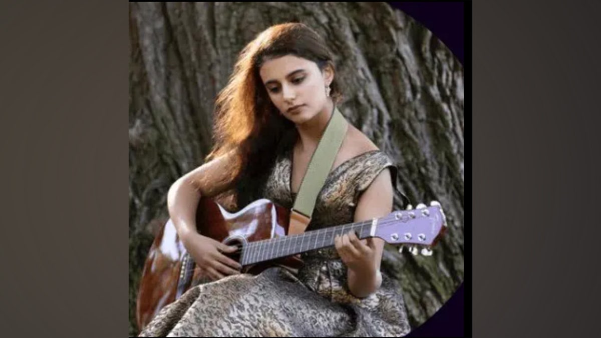 Mujer toca la guitarra junto a un árbol.