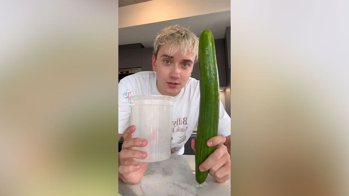 Man holding an entire cucumber at the camera.