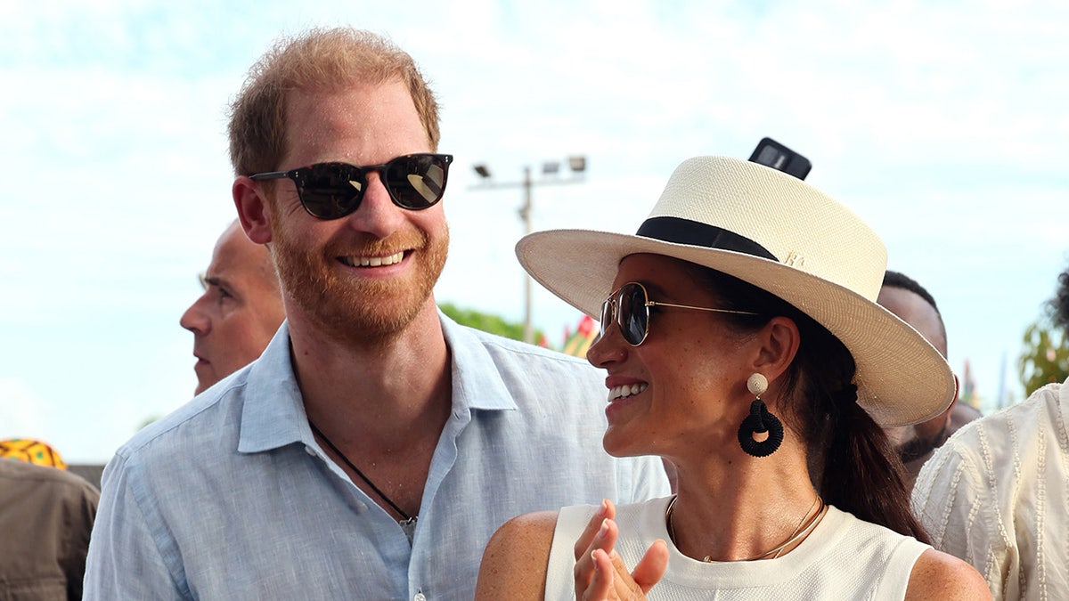 El príncipe Harry y Meghan Markle llevan gafas de sol y sonríen