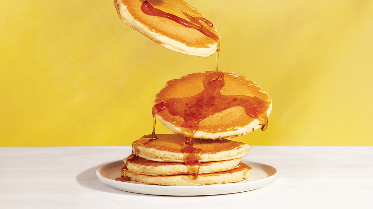 A pancake stack that has the apical  2  pancakes falling connected  to the stack with syrup showing.