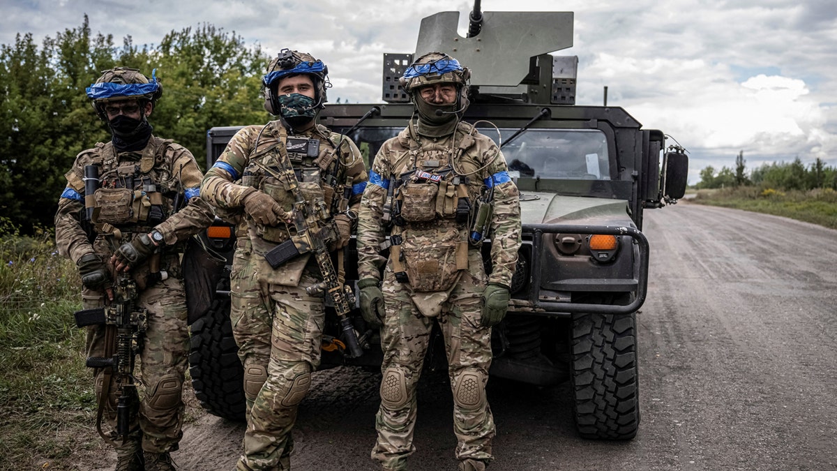 Ukrainian servicemen stand in front of a military vehicle