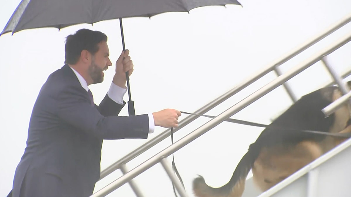 JD Vance smiles as his dog Atlas pulls him up stairs to a plane