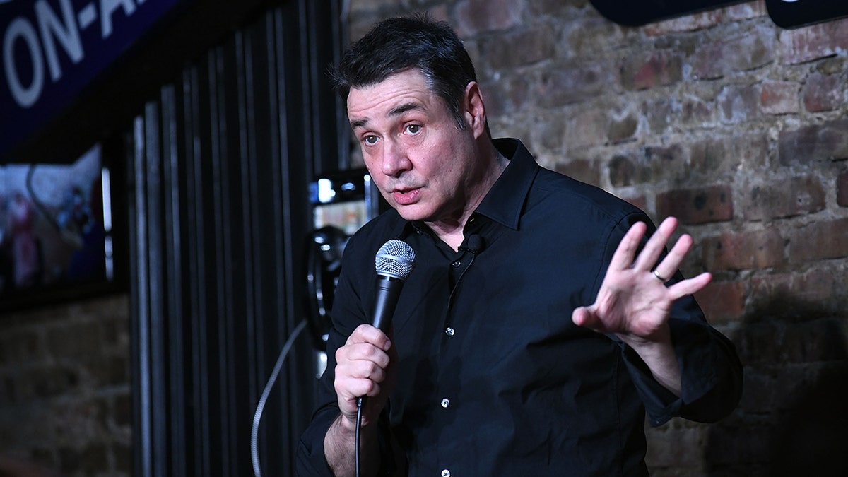 Adam Ferrera in a navy shirt performs on stage holding a microphone