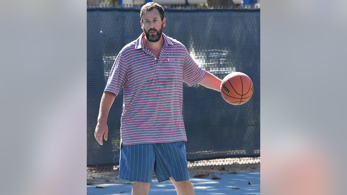 Adam Sandler in a striped collar shirt and striped shorts plays basketball in Los Angeles