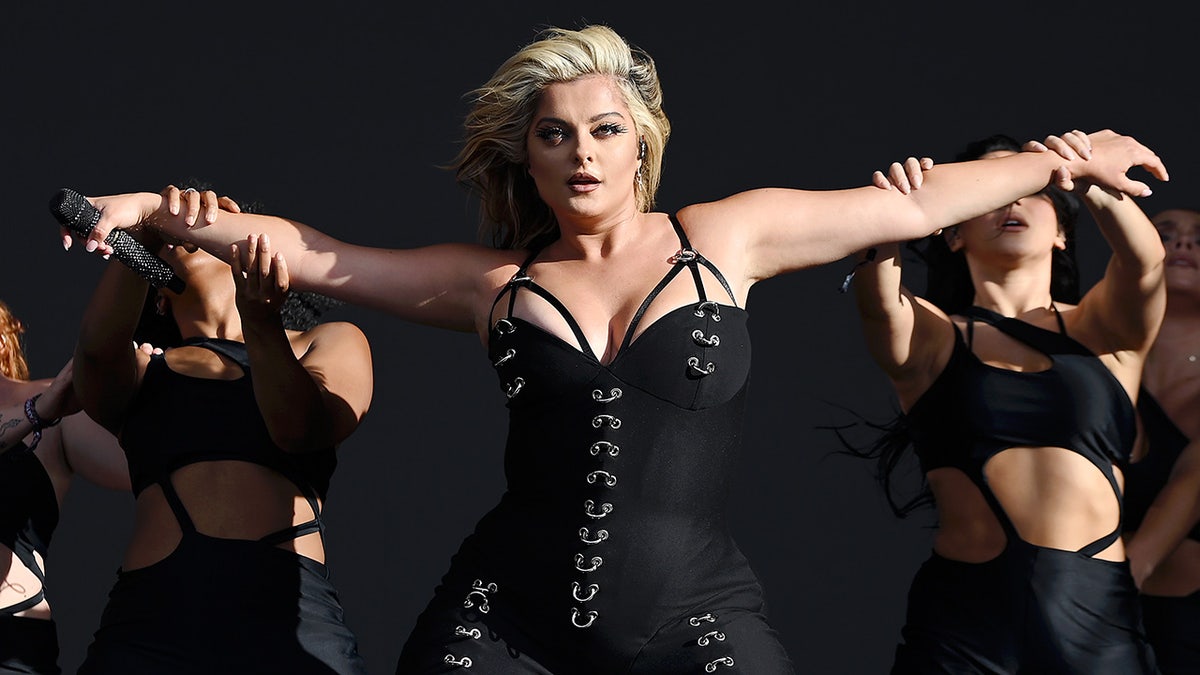 Bebe Rexha wears a black strappy corset and extends her arms on stage