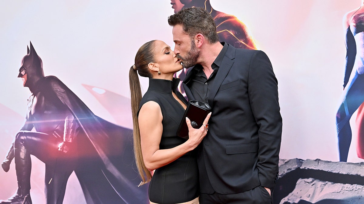 Jennifer Lopez in a black dress and long ponytail kisses husband Ben Affleck in a black suit on the carpet