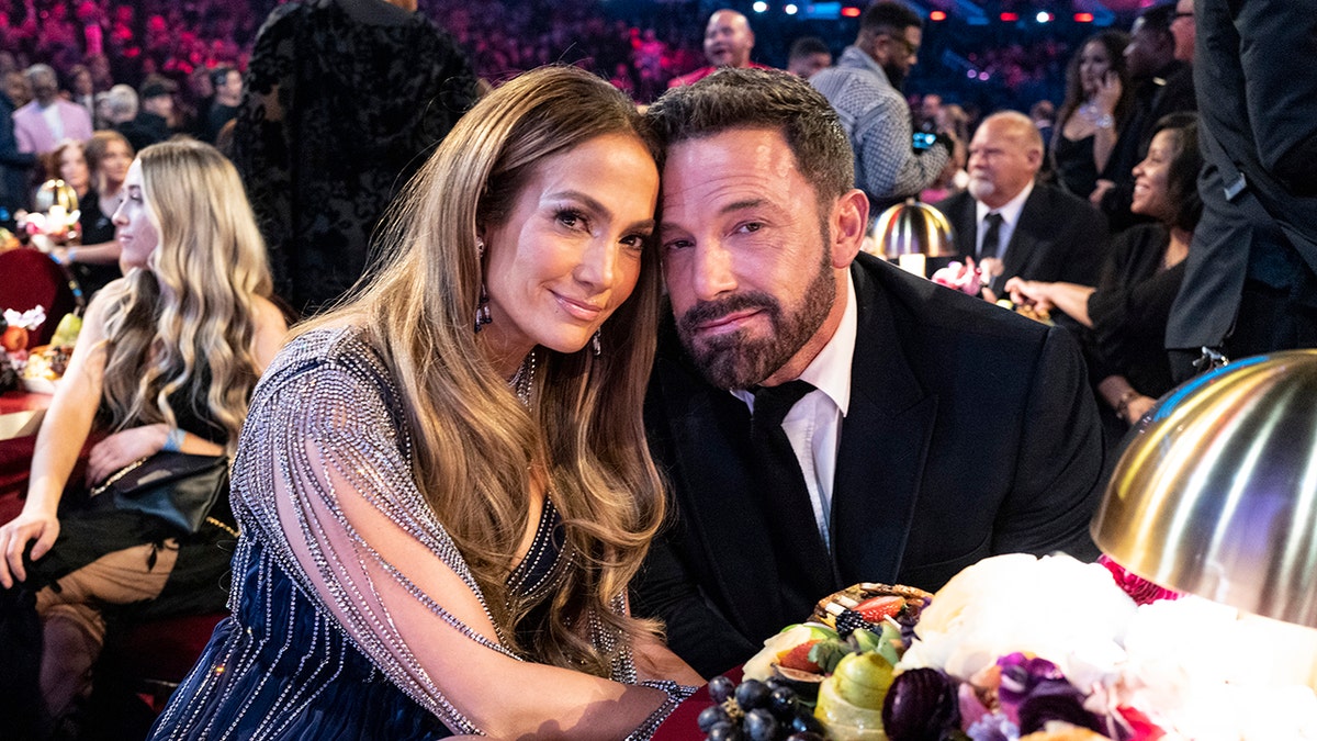 Jennifer Lopez em um vestido azul com mangas transparentes sorri suavemente com o marido Ben Affleck em um terno preto no Grammy