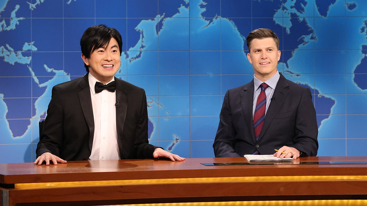 Bowen yang lleva traje mientras bromea con Colin Jost