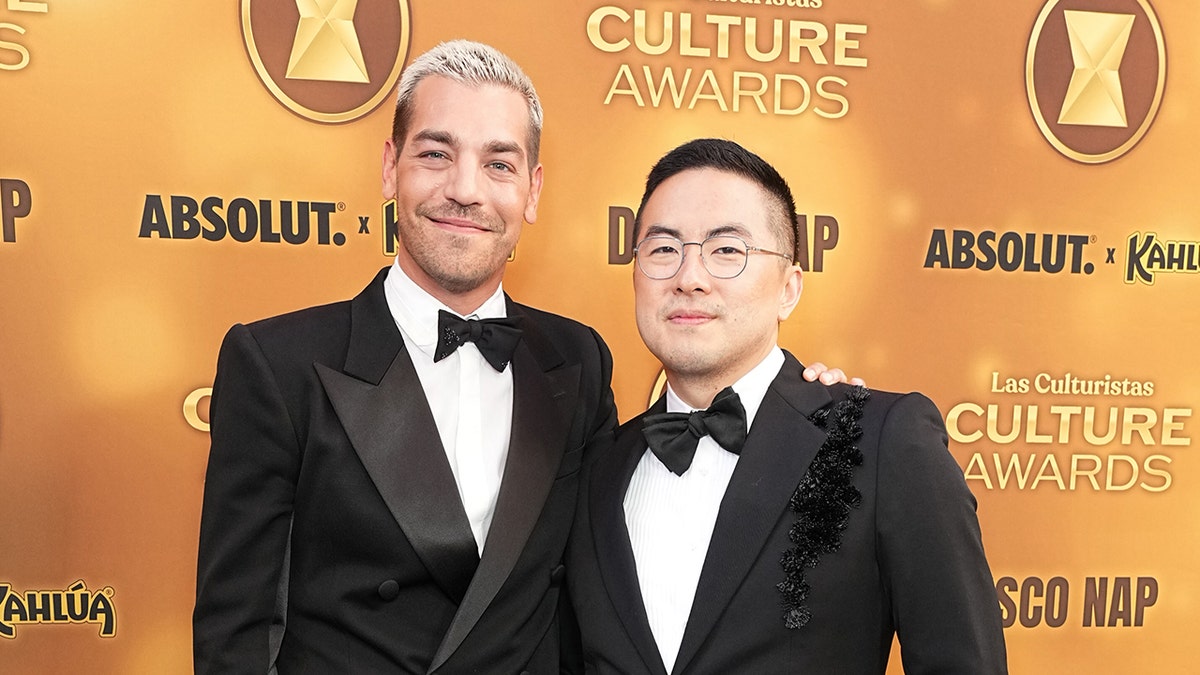 Bowen Yang and Matt Rogers wear black suits at podcast awards.