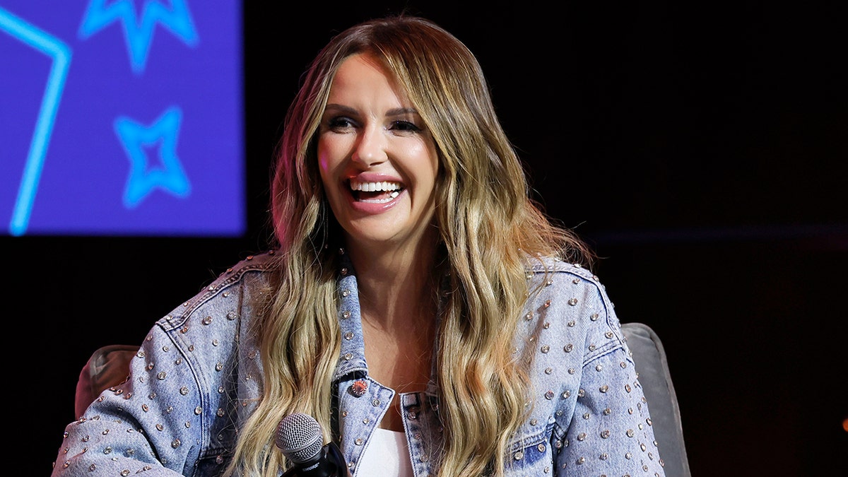 Carly Pearce laughs on stage in a jean studded jacket