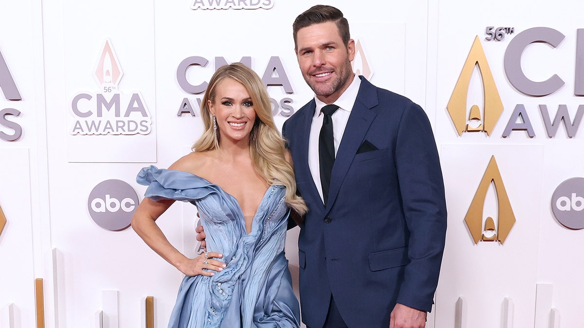 Carrie Underwood in a blue dress with a plunging neckline poses with husband Mike Fisher in a blue suit on the CMA Awards carpet