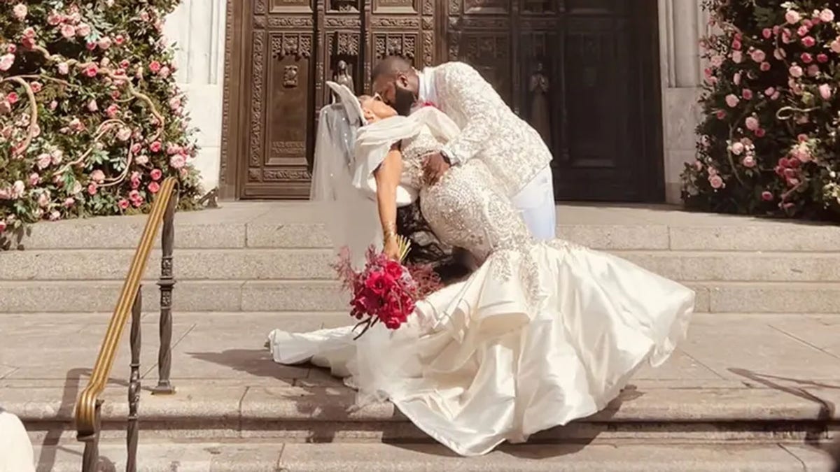 Man and woman in elaborate wedding regalia kissing in front of church doors.