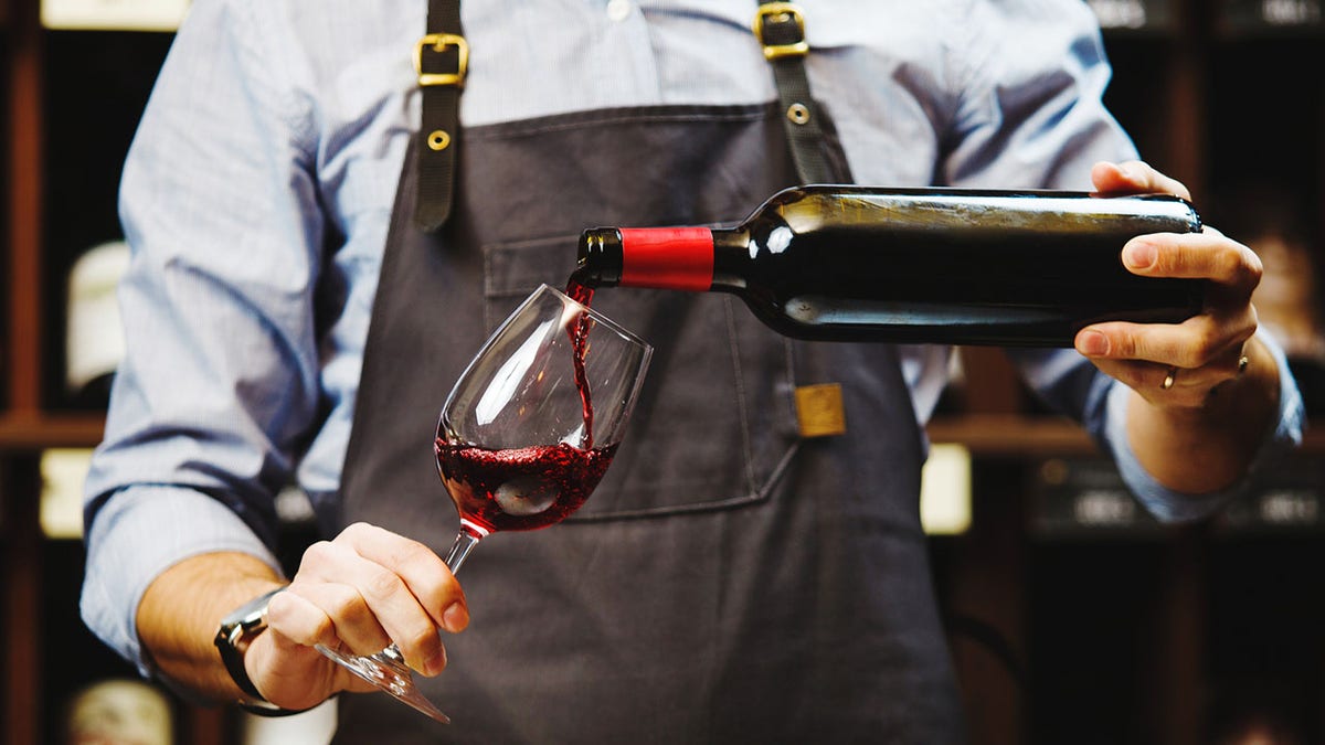 Male sommelier pouring red wine into long stemmed wine glasses.