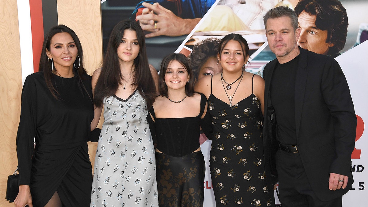 Luciana Damon in black poses for a photo on the carpet with her daughters Issabella, Stella and Gia and her husband Matt Damon in a black suit