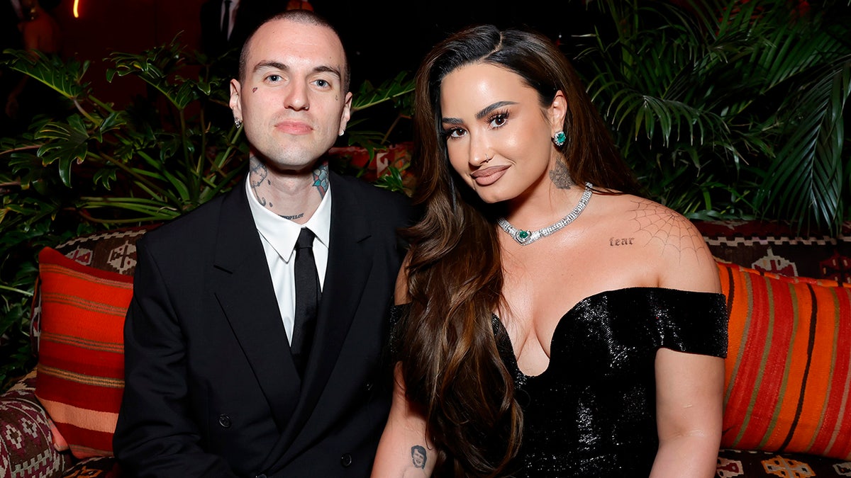 Jordan Lutes, con traje negro y corbata, sonríe suavemente con Demi Lovato, con un vestido negro sin hombros, en la fiesta de los Oscar de Vanity Fair.