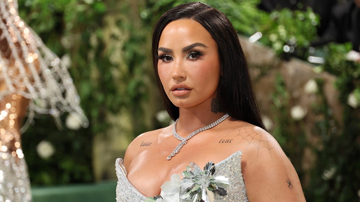 Demi Lovato con un vestido plateado de lentejuelas con detalles florales mira directamente a la cámara en la alfombra de la Gala del Met