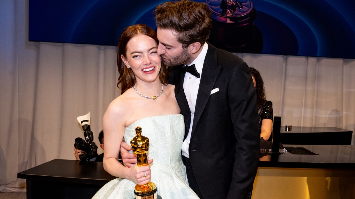 Emma Stone sostiene el Oscar mientras su marido Dave McCary le besa la mejilla