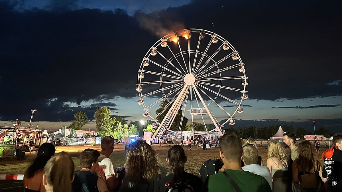 Spectators watch as the Ferris wheel continues to burn.