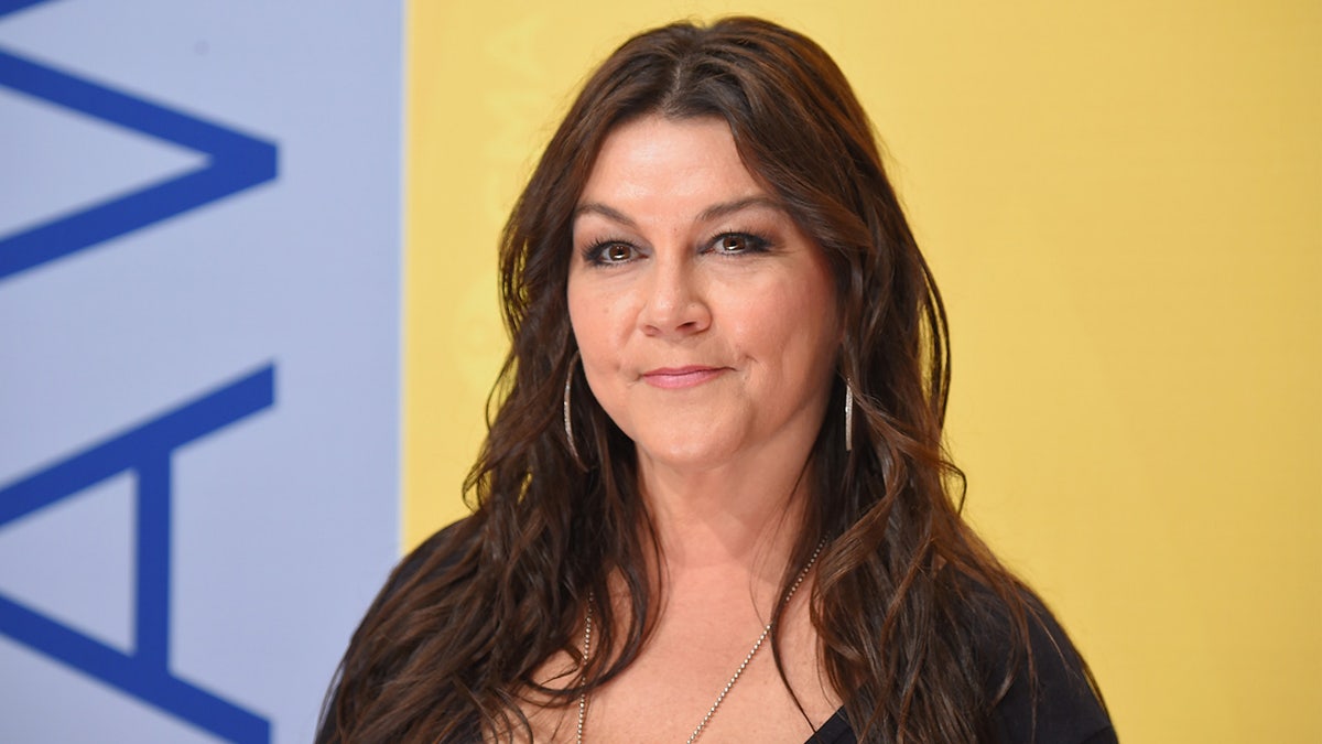 Gretchen Wilson em um top preto parece séria no tapete