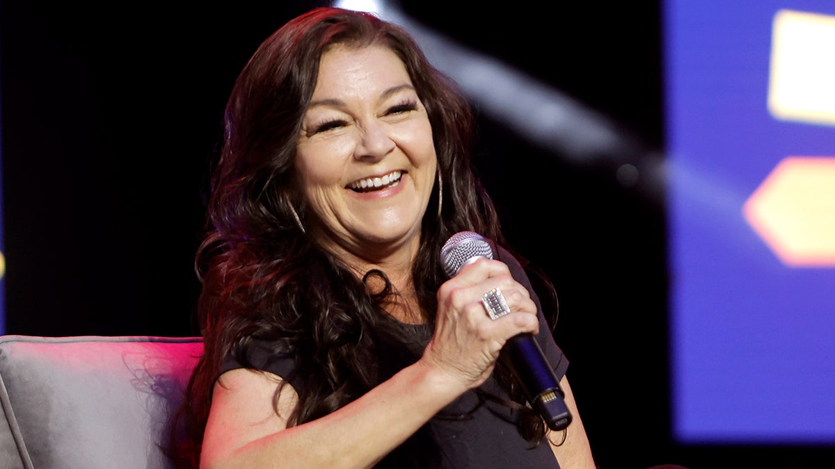 Gretchen Wilson holds the microphone on stage and laughs while sitting down